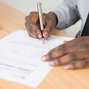 Close-up of a businessman signing a contract at an office desk.